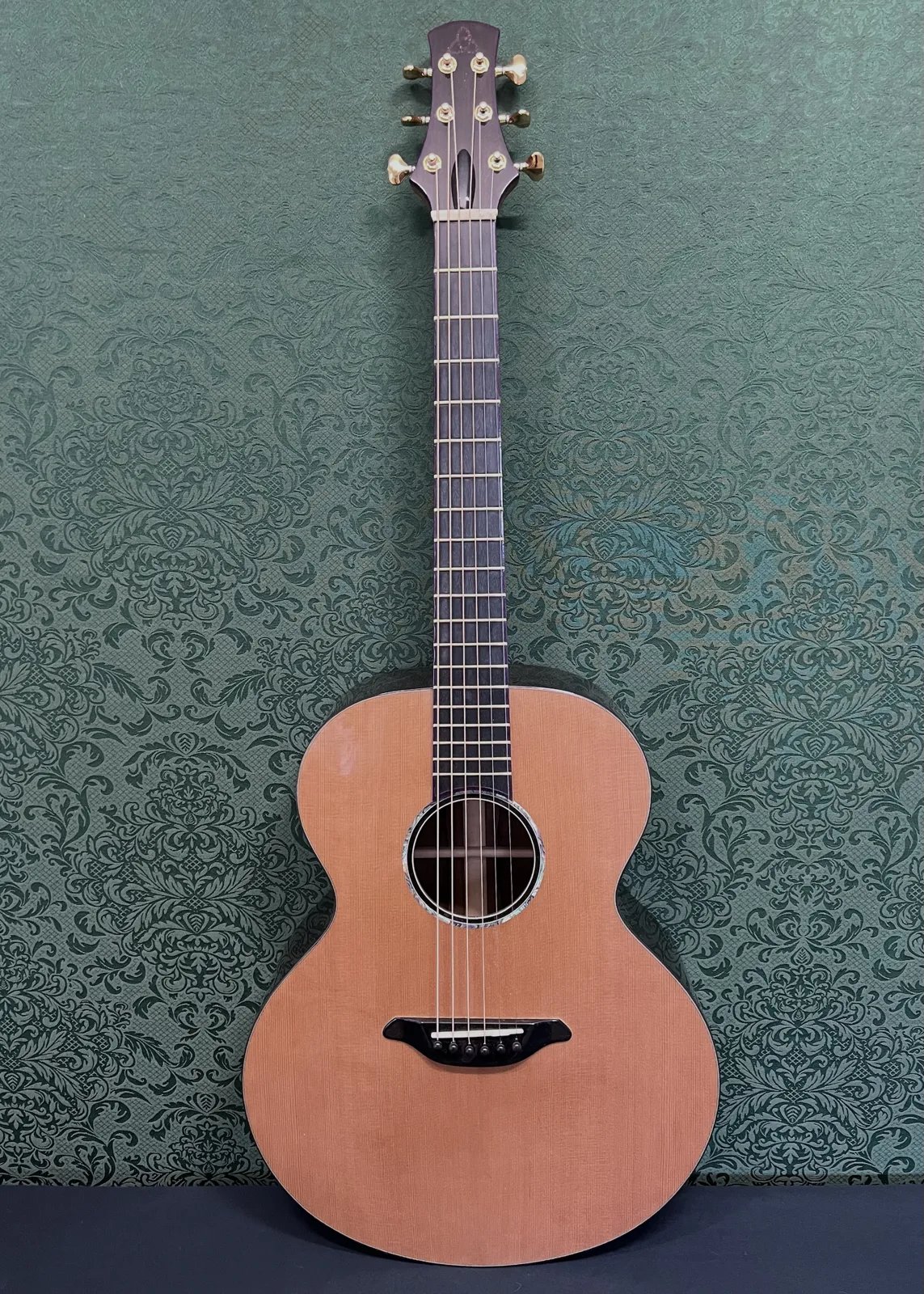 Front of Build No. 001: cedar top, abalone rosette, black bridge and gold tuners, against a green damask wall