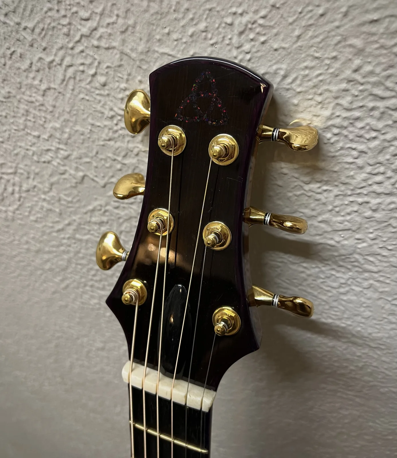 The headstock: dark purple-edged face with a sparkling triquetra inlay and gold tuners