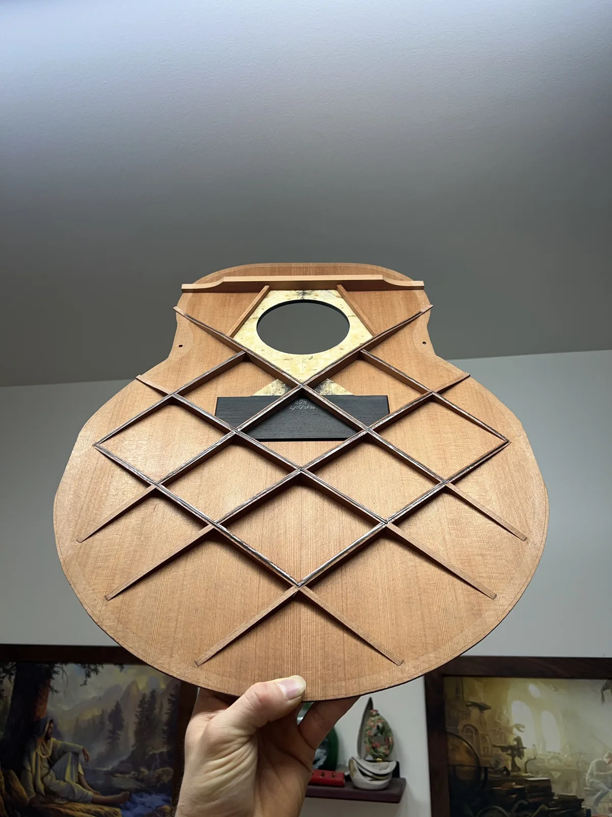 The cedar top held up to show its lattice bracing, burl rosette patch and an ebony bridge plate signed and dated