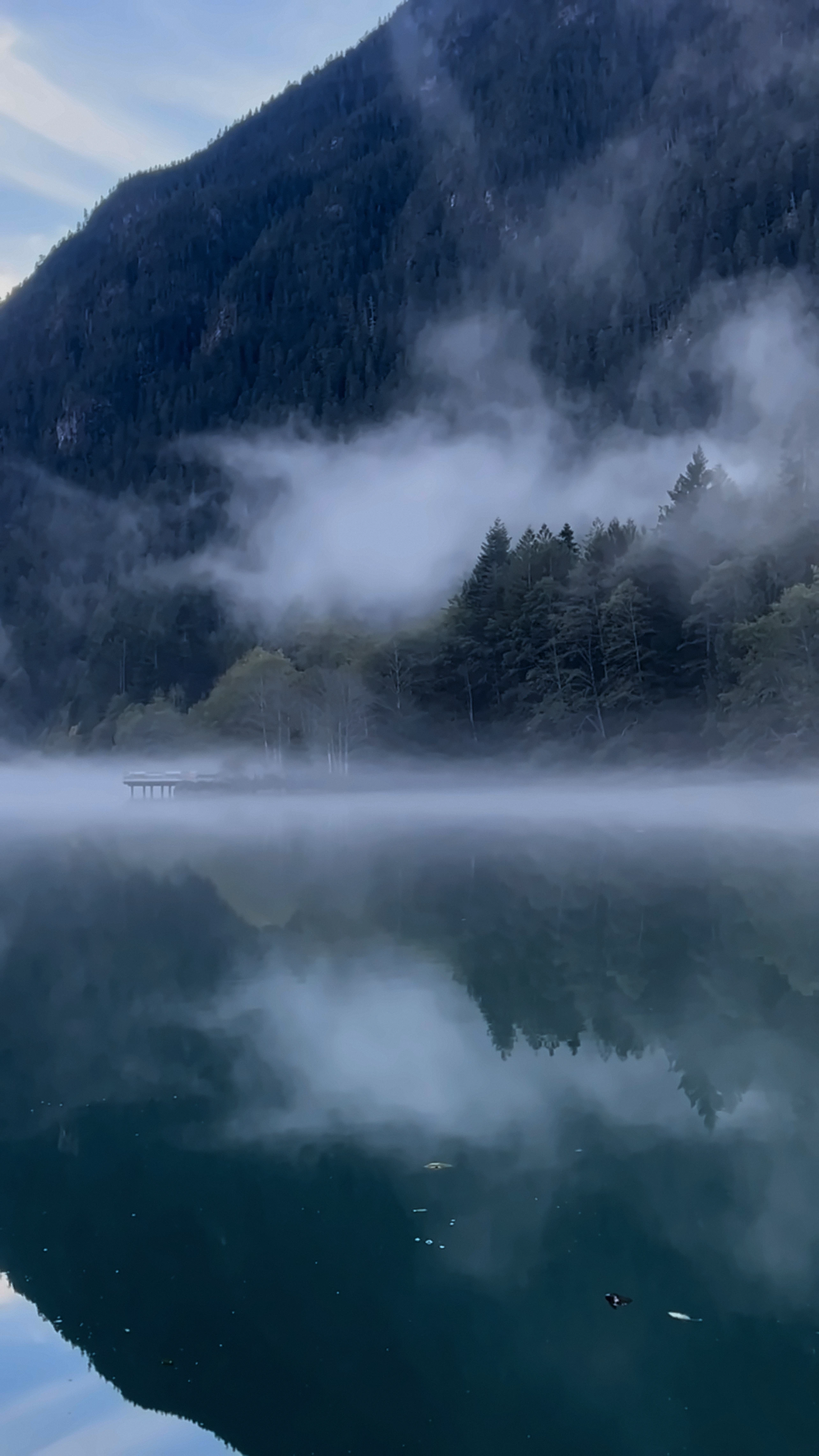 Fog lifting off a still mountain lake in the North Cascades, trees reflected in the water
